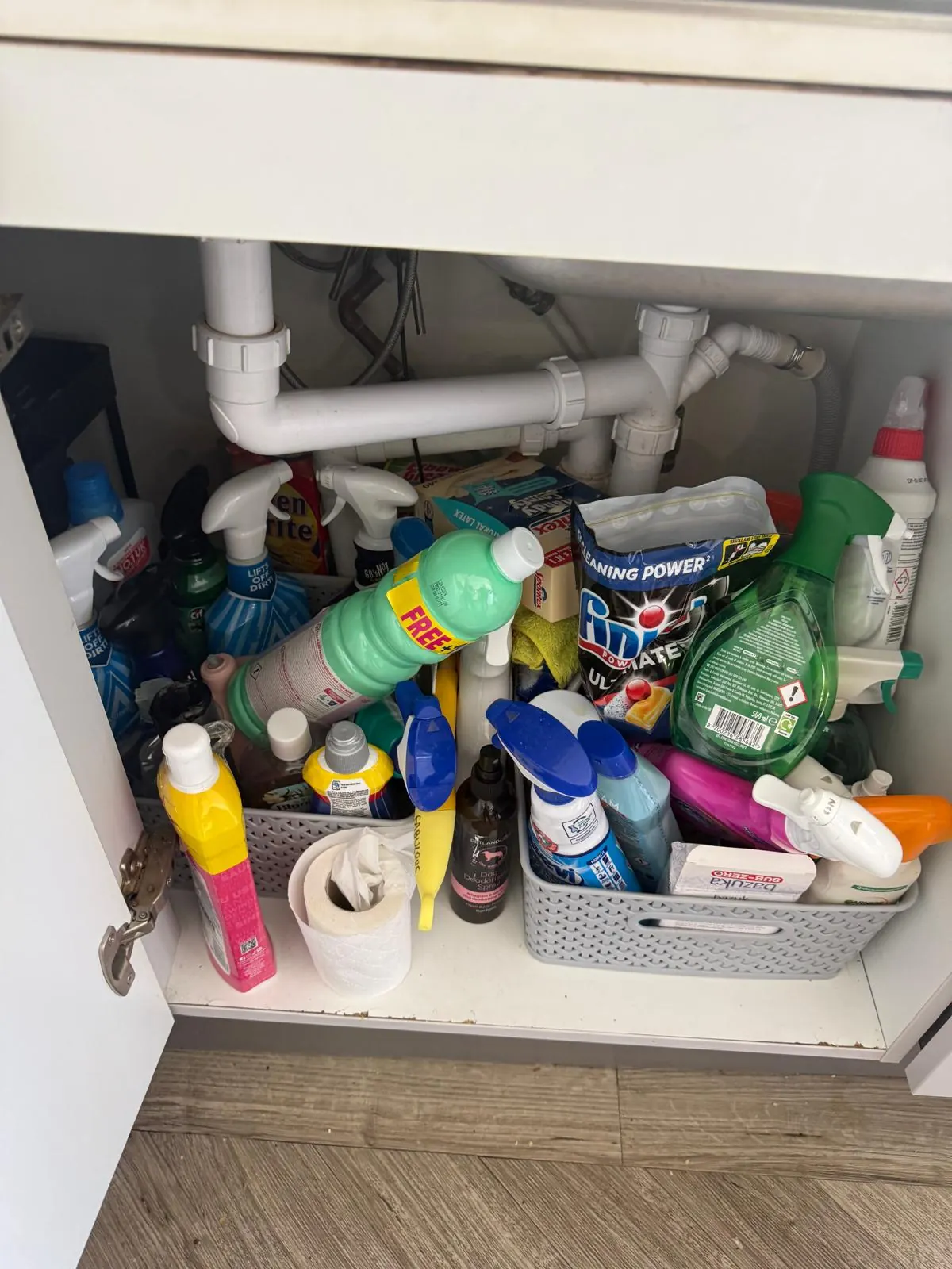 Overfilled under-sink cupboard before organising, with cleaning bottles piled up