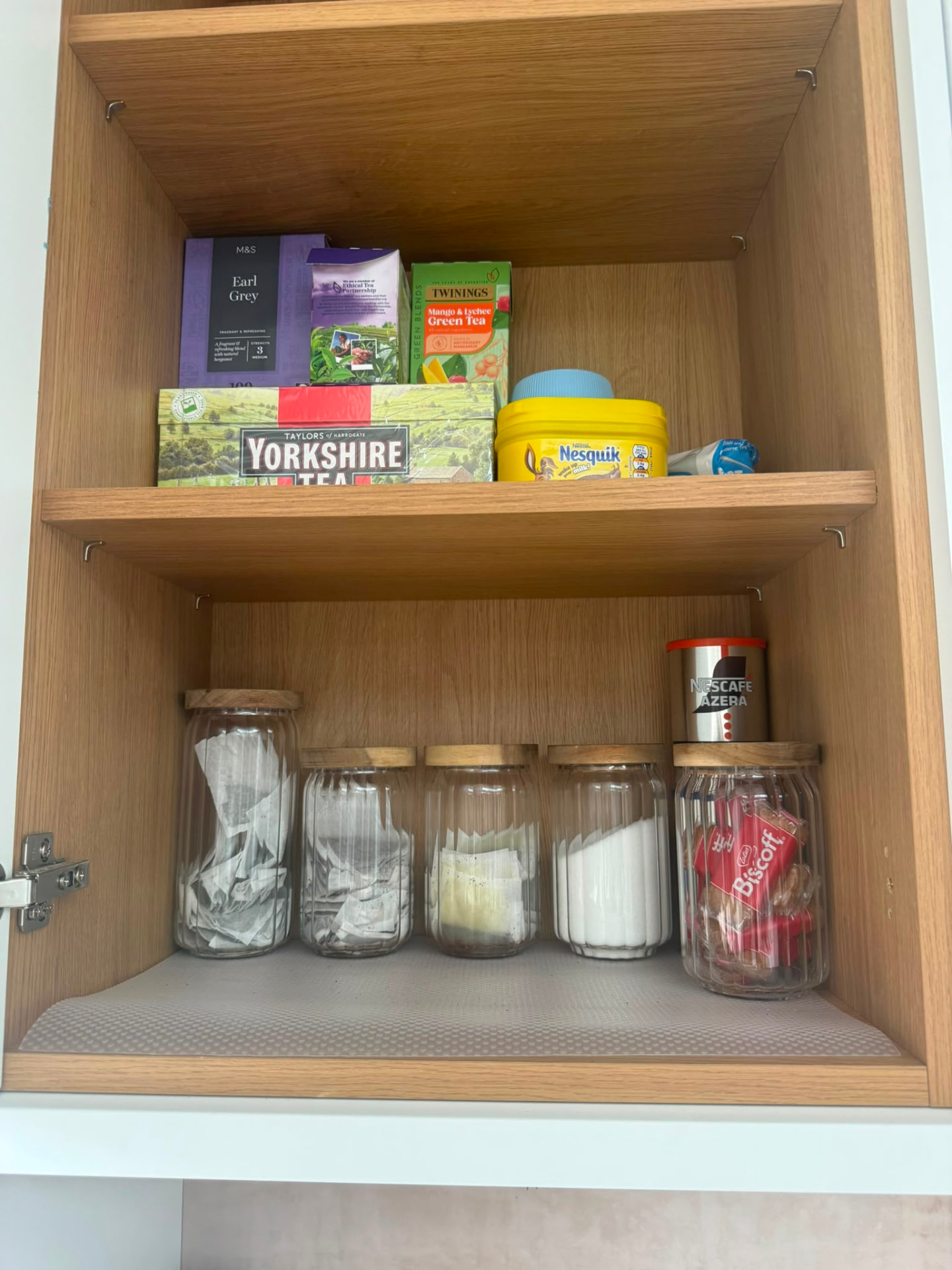 Organised tea and coffee cupboard with glass jars and neatly stacked boxes