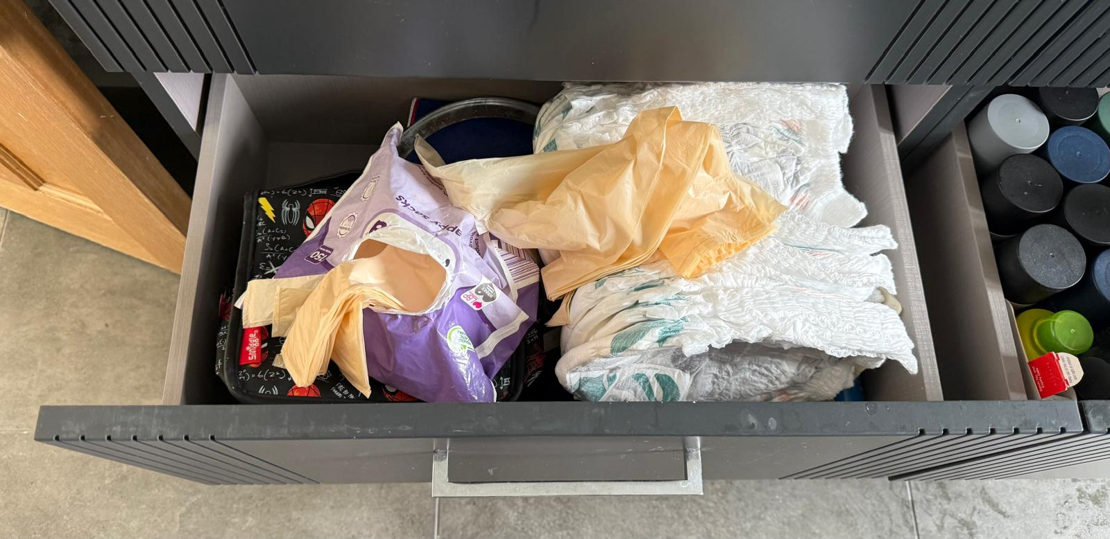 Cluttered kitchen drawer before organising, with loose bags and nappies