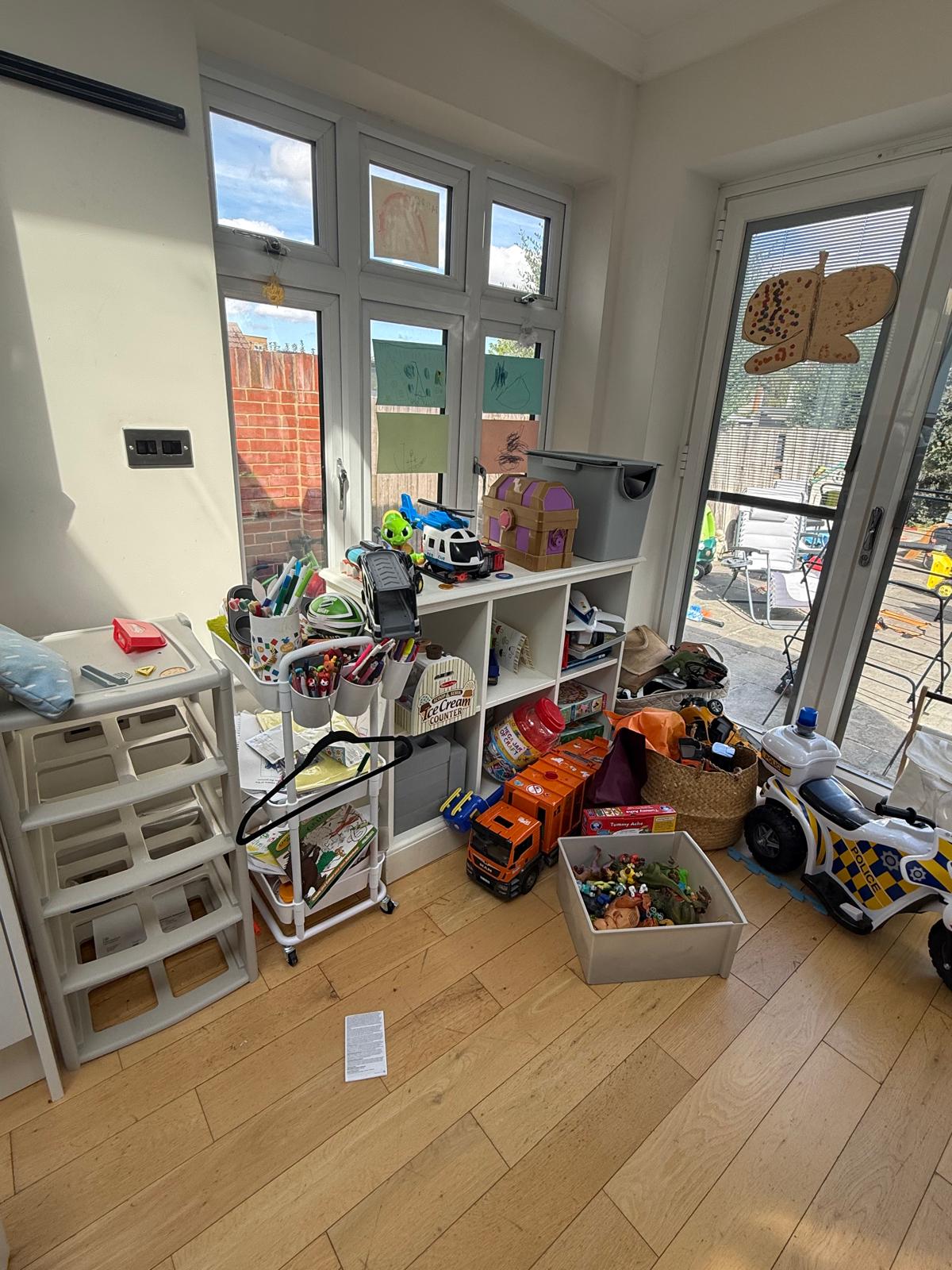 Children's playroom corner before organising, with toys, craft trolley and boxes crowding the floor