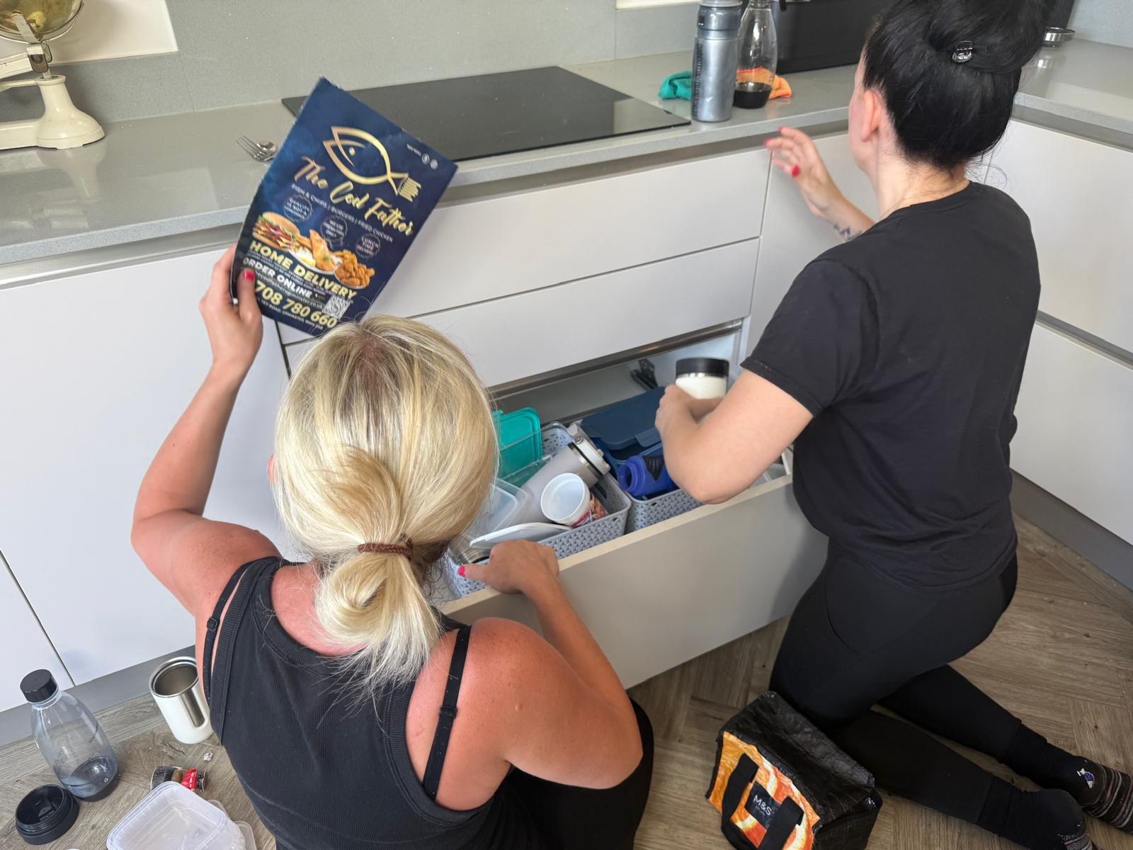 Two professional organisers unpacking and arranging kitchen drawers in a new home