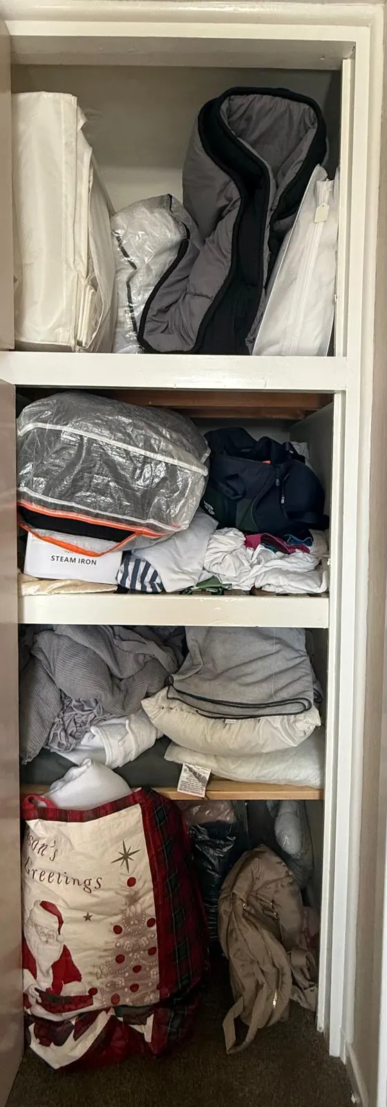 Airing cupboard before organising, with bedding, coats and bags crammed onto the shelves