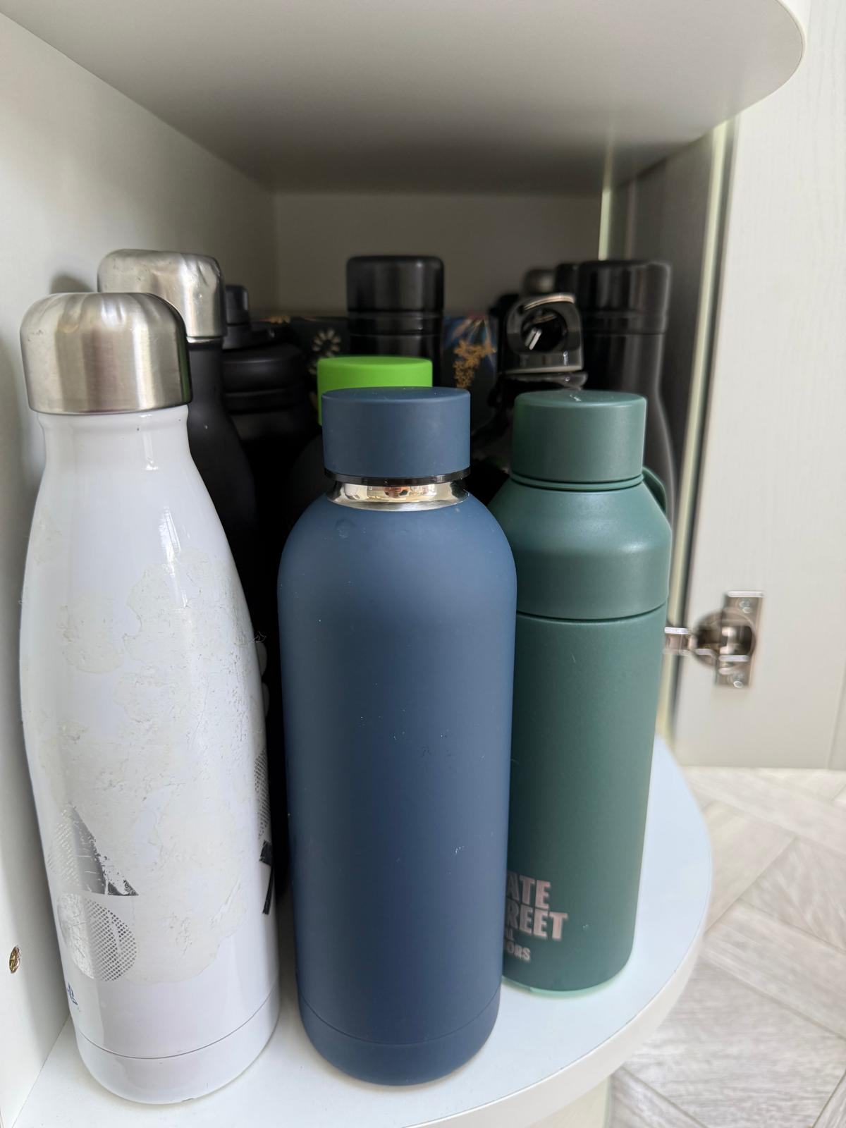Same cupboard after organising, with water bottles cleaned and stood in neat rows