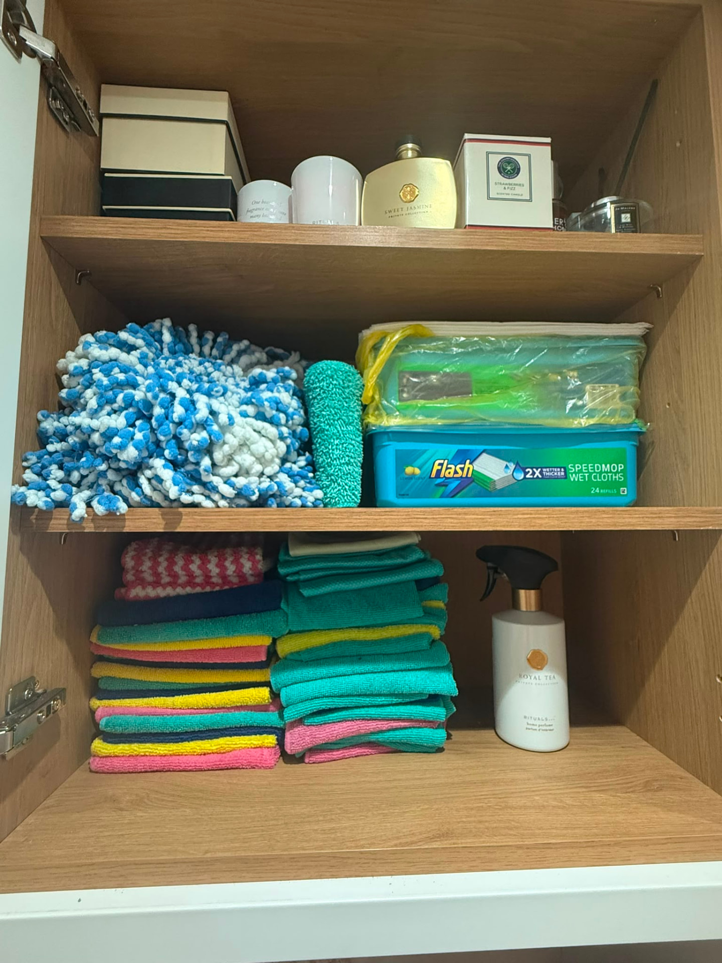 Organised utility cupboard with folded cleaning cloths and cleaning supplies neatly zoned across wooden shelves in an Essex home