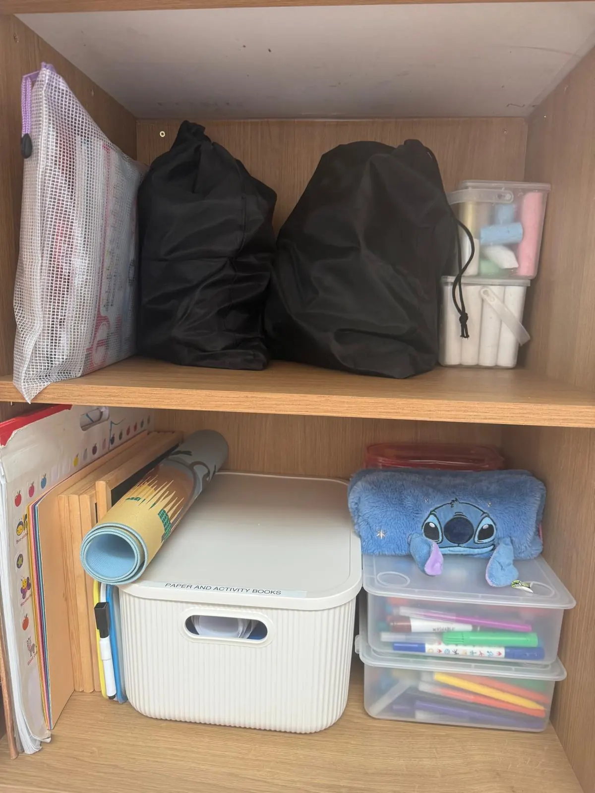 Craft cupboard after organising, with labelled boxes for paper, activity books and pens