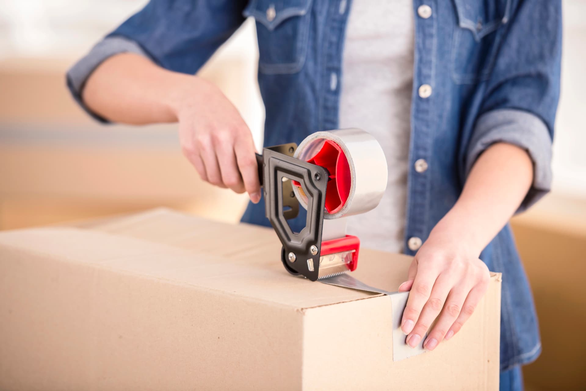 Person sealing a cardboard box with tape, ready for unwanted items to be collected and removed