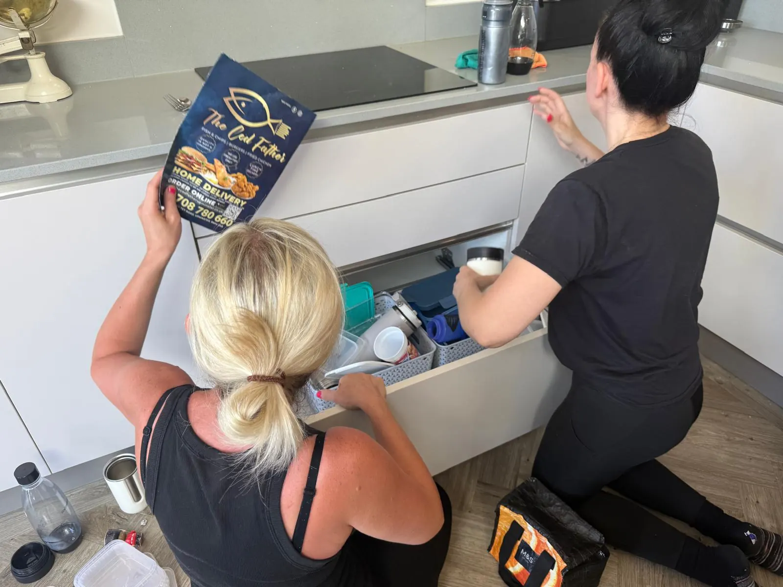 Two professional organisers unpacking and arranging kitchen drawers in a new home