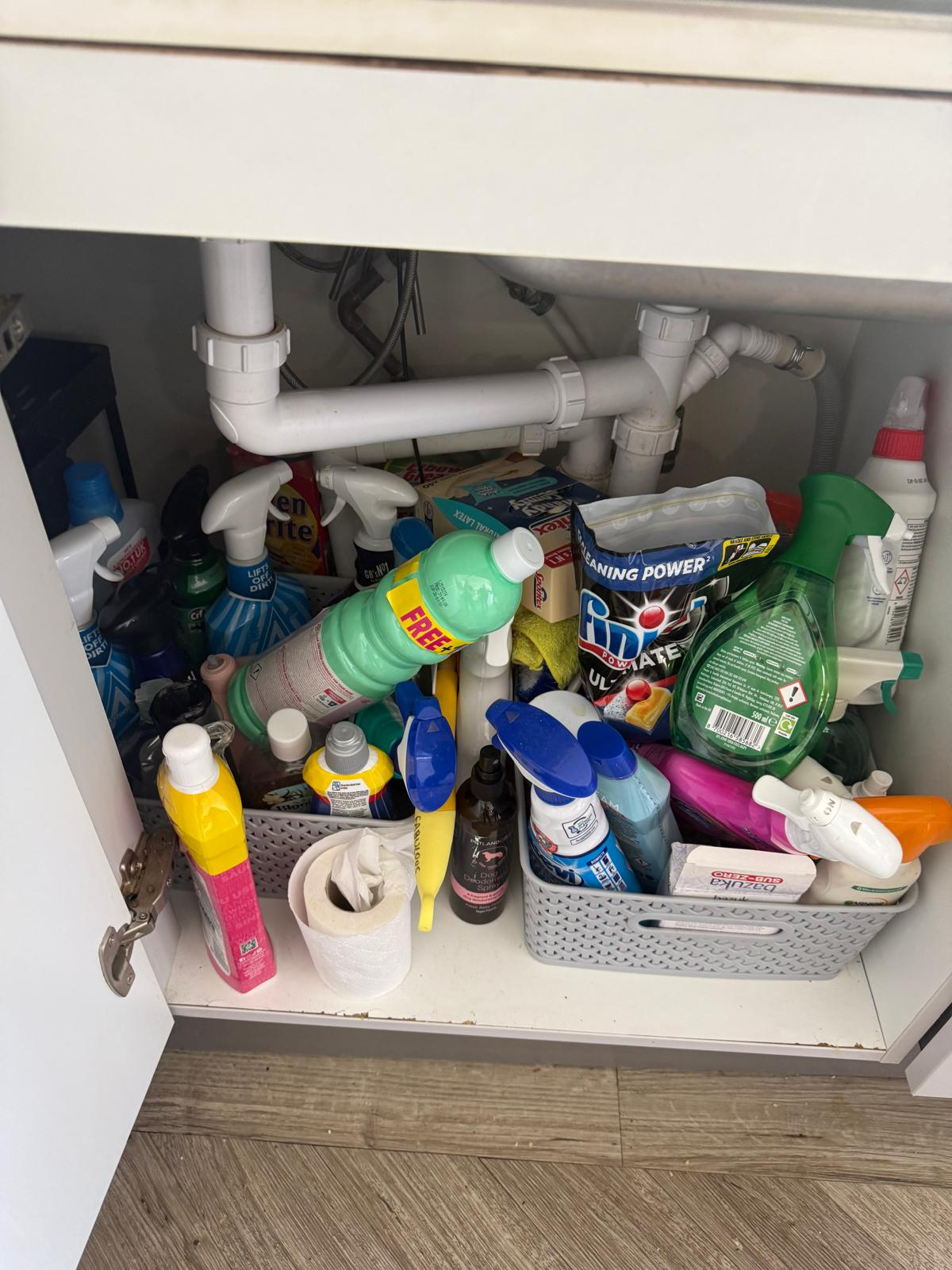 Overfilled under-sink cupboard before organising, with cleaning bottles piled up