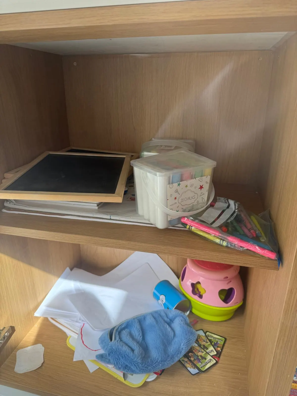 Craft cupboard before organising, with paper, chalks and pens loose on the shelves