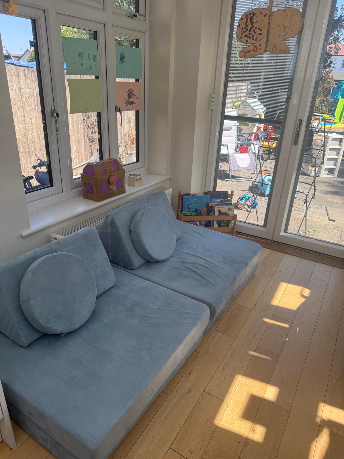 Playroom corner after organising, with a clear floor, soft play seating and a tidy book rack