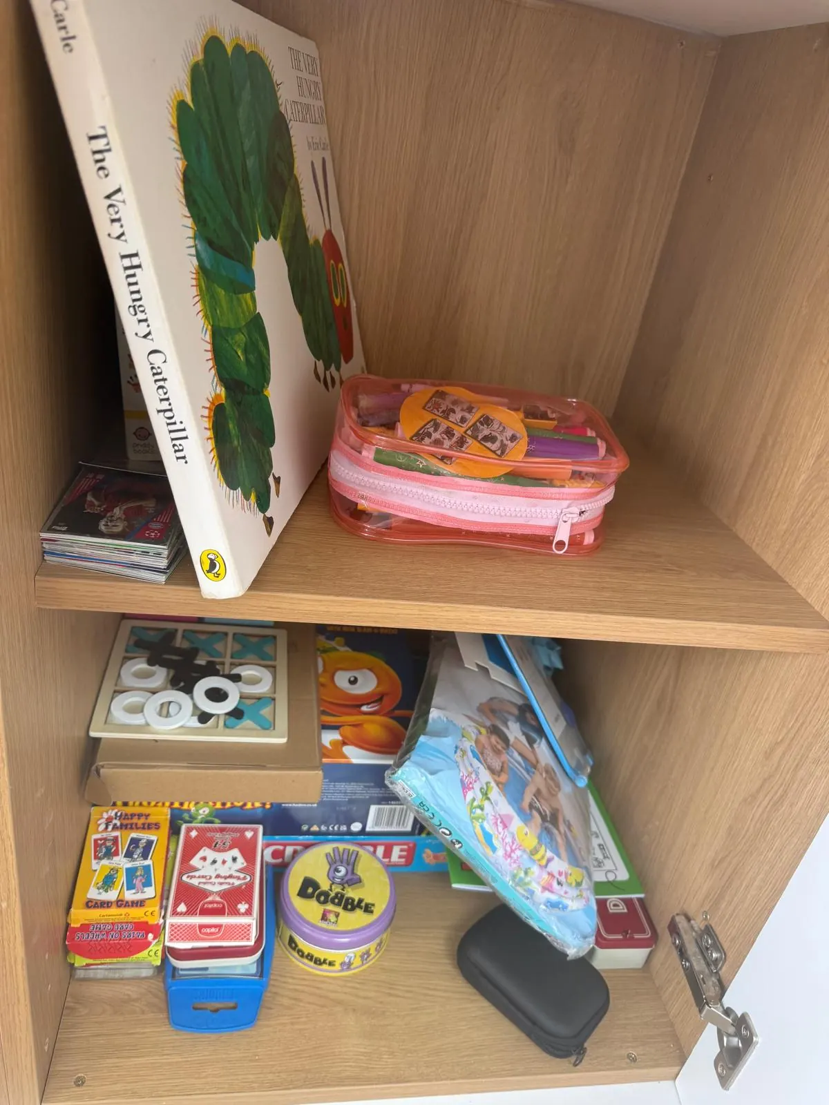 Children's games cupboard before organising, with books and games stacked loosely