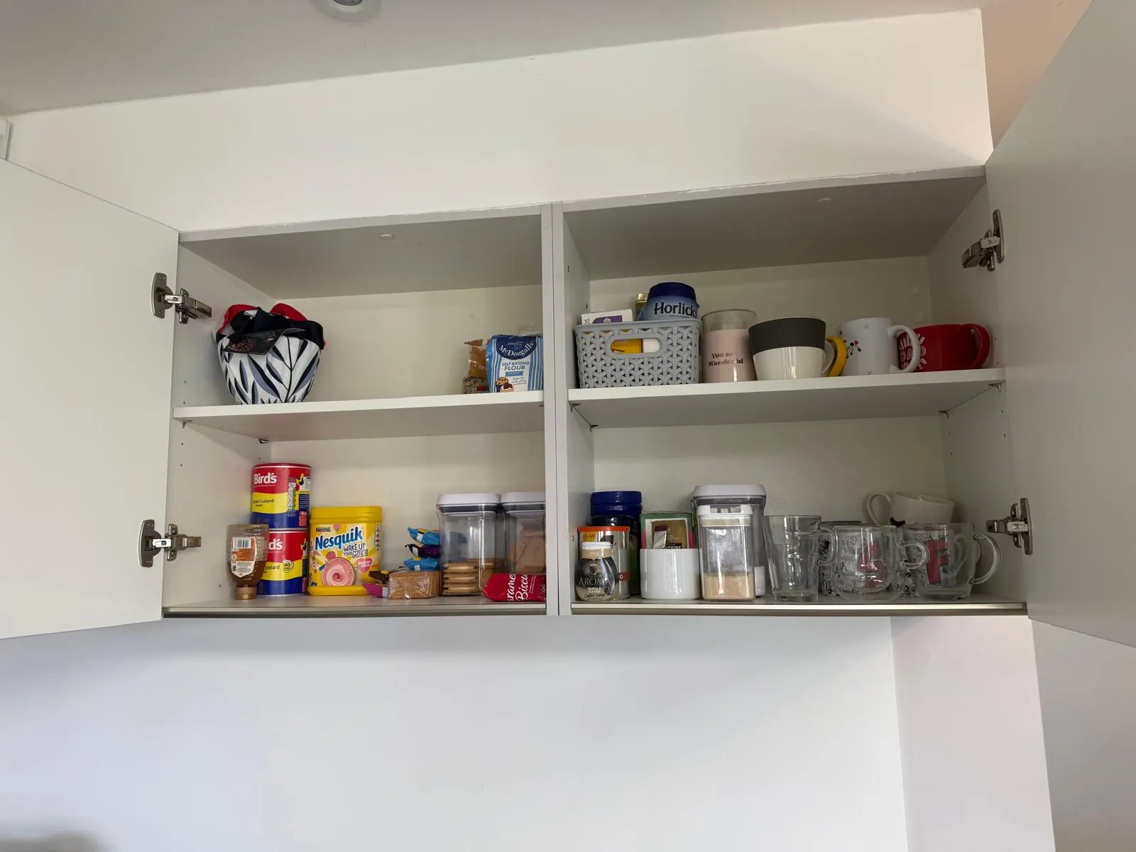 Organised kitchen wall cupboard with baking supplies, mugs and labelled containers