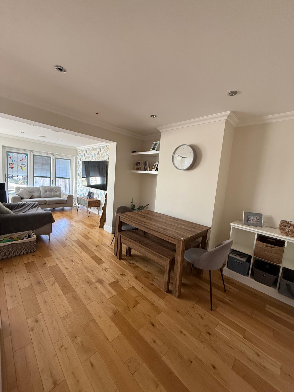 Open-plan dining and living room after organising, with clear floors, a tidy table and baskets on the shelving unit