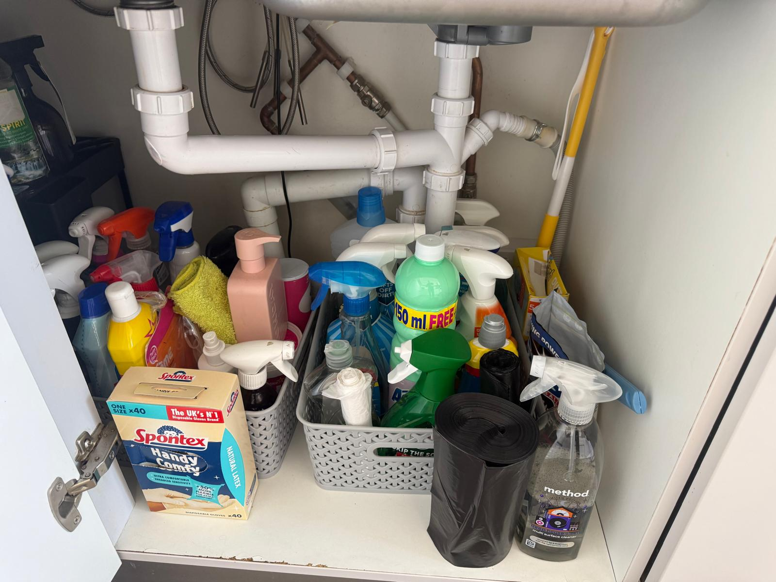 Under-sink cupboard after organising, with cleaning products sorted into baskets