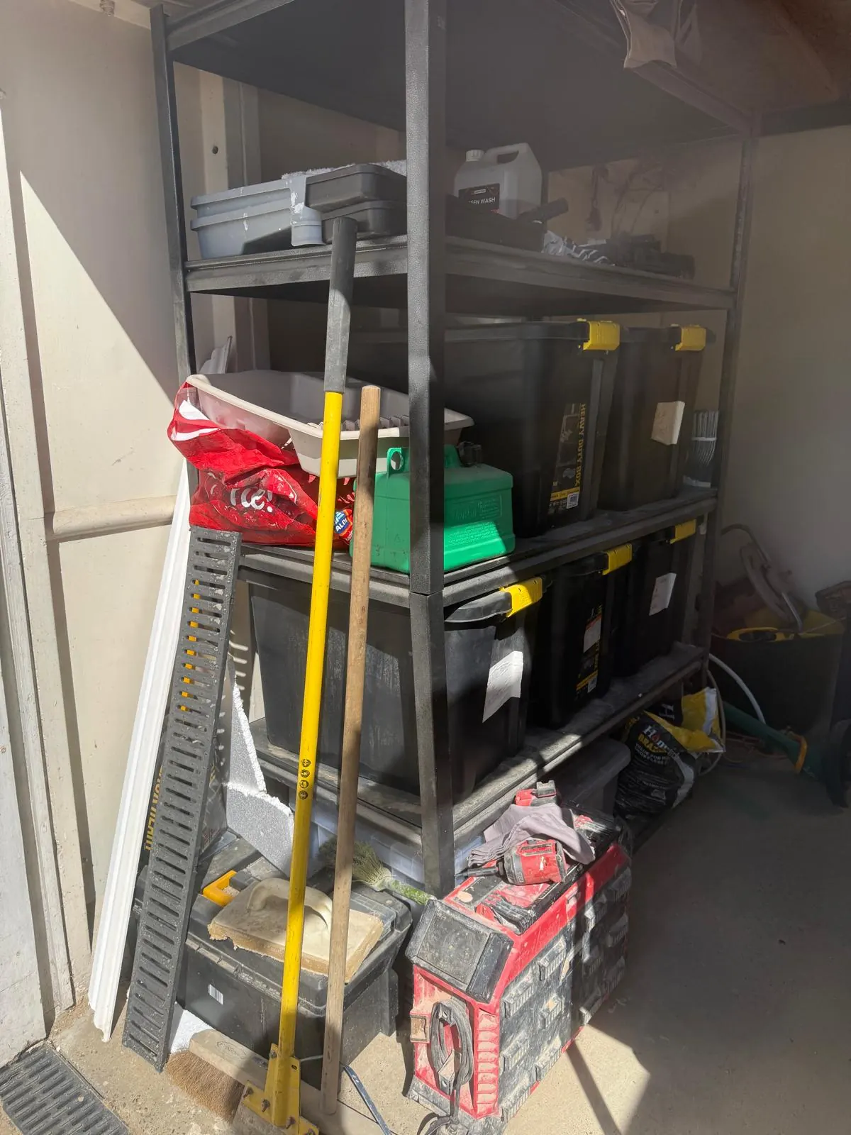Garage shelving before organising, with tools, bags and boxes stacked across the floor