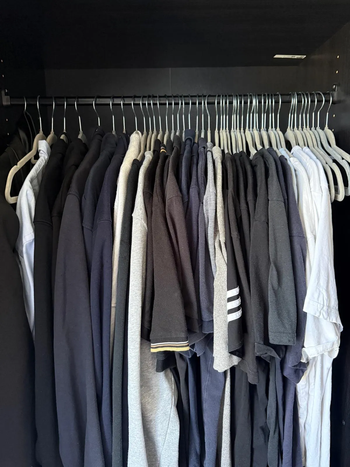 Organised wardrobe rail with shirts and tops sorted by colour on matching hangers