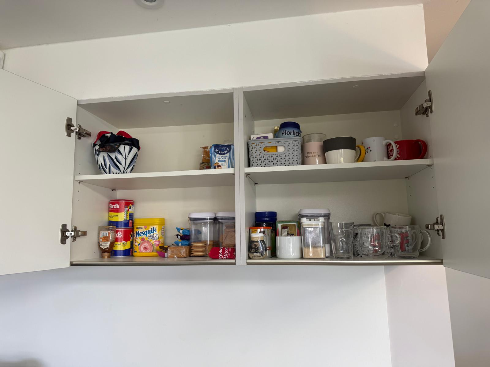 Organised kitchen wall cupboard with baking supplies, mugs and labelled containers