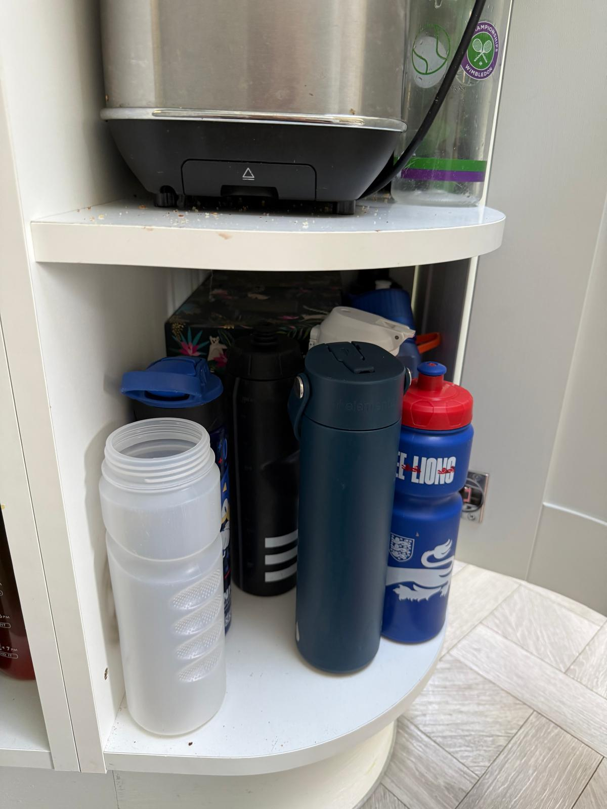 Kitchen corner cupboard before organising, with water bottles crammed in and crumbs on the shelf