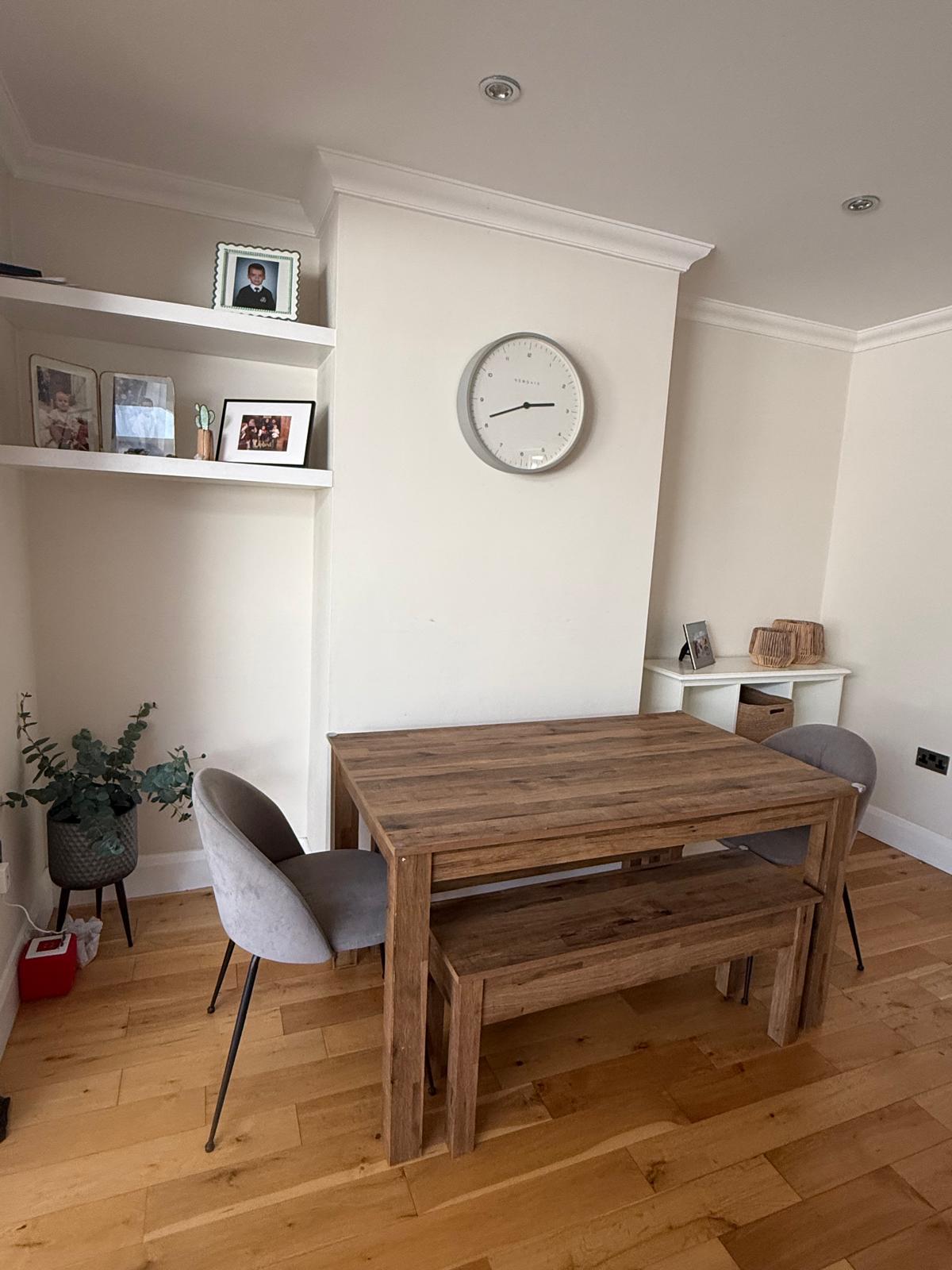 Calm dining area with a wooden table, bench, styled shelves and clear floor space